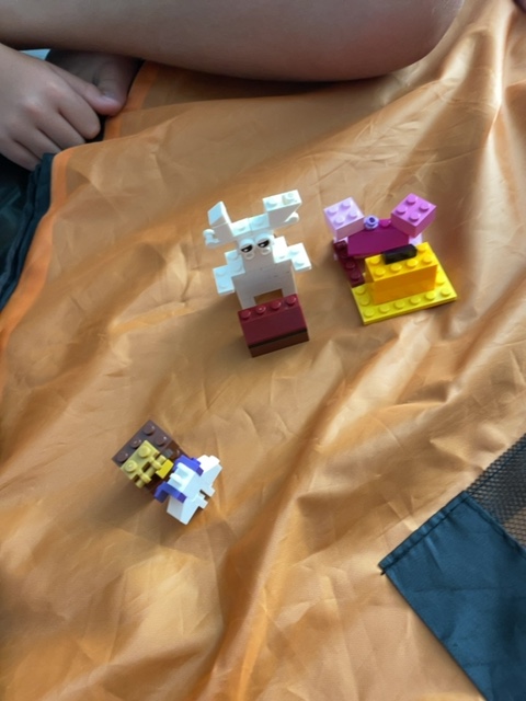 A Fast Brix! gallery build by @mtt for the #BunnyPullingTreasure prompt: a white and maroon LEGO bunny with big ears next to a pink and yellow treasure chest, plus a tiny third character, all on an orange blanket.